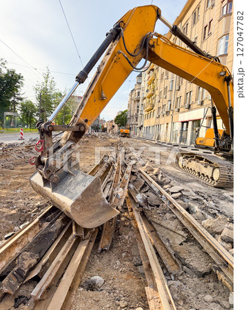 Excavator removing old tram rails at sunset. Urban transportation renewal in progress. 127047782
