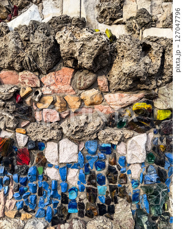 Colorful stone and glass mosaic embedded in textured concrete wall. The image explores craftsmanship and tactile urban detail 127047796