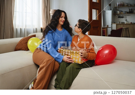 A woman and child celebrate with balloons and a gift in a cozy living room A woman and child celebrate with balloons and a gift in a cozy living room 127050037