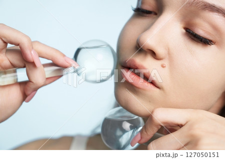 Elegant woman examining skin using magnifying glass in bright setting 127050151