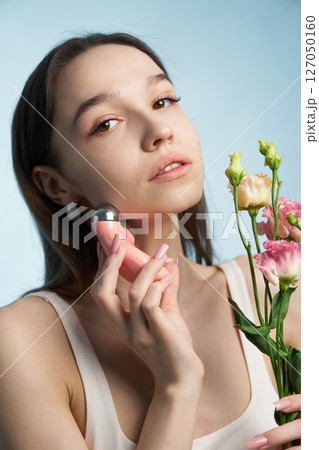 Woman using skincare tool while holding bouquet in bright atmosphere Woman using skincare tool while holding bouquet in bright atmosphere 127050160