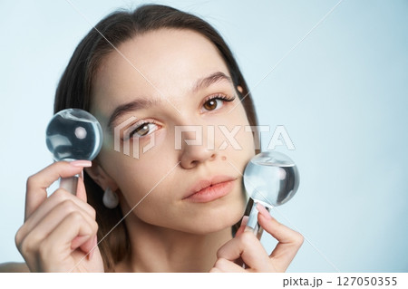 Woman holding magnifying glasses while posing against light blue backdrop 127050355