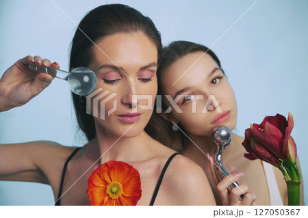 Two women practicing skincare with flowers in a bright studio setting Two women practicing skincare with flowers in a bright studio setting 127050367