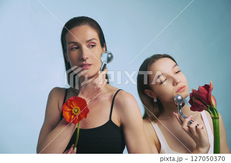 Two women enjoying skincare routine with facial tools and flowers 127050370
