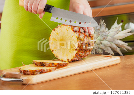 Woman chopping fresh pineapple on cutting board... Woman chopping fresh pineapple on cutting board... 127051383