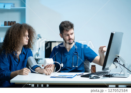doctor checking woman blood pressure at clinic and filling patient history. doctor checking woman blood pressure at clinic and filling patient history. 127052584