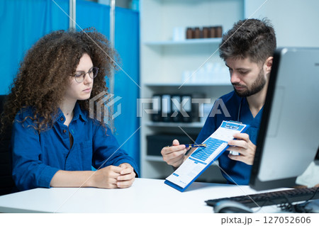 Male doctor consulting patient filling form at consultation, talking to woman patient filling signing medical paper at appointment visit in clinic. Male doctor consulting patient filling form at consultation, talking to woman patient filling signing medical paper at appointment visit in clinic. 127052606