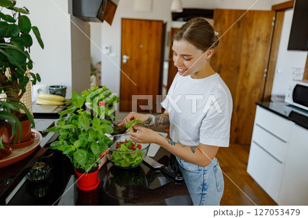 A Young Woman Diligently Caring for Her Indoor Plants in a Beautiful Modern Kitchen Setting 127053479