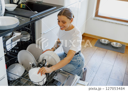 A woman loads dishes into the dishwasher at her cozy home, making chores easier 127053484
