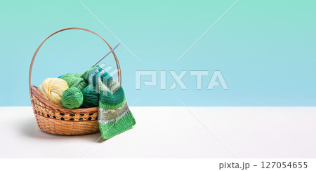 Green knitting balls in a basket with knitting needles on beige table. Set for the hobby of knitting warm clothes or toys. Concept needlework. Banner Green knitting balls in a basket with knitting needles on beige table. Set for the hobby of knitting warm clothes or toys. Concept needlework. Banner 127054655