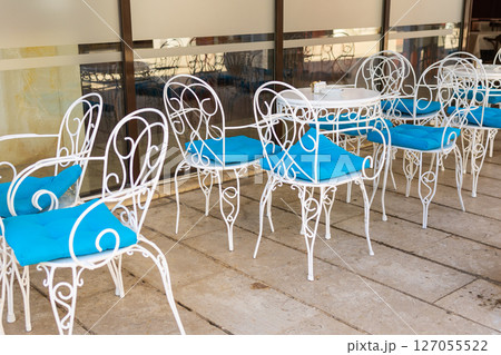 Chairs and table by glass wall. Outdoor restaurant, summer hospitality, and Mediterranean cafe design in quiet courtyard. 127055522