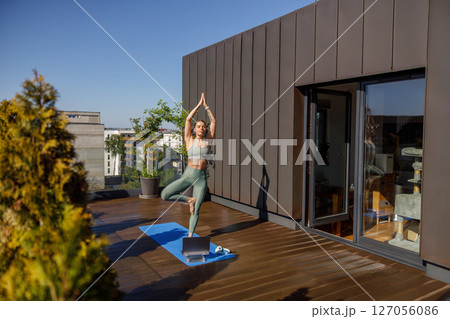 A woman practicing yoga on a stunning rooftop while enjoying a beautiful and serene view A woman practicing yoga on a stunning rooftop while enjoying a beautiful and serene view 127056086