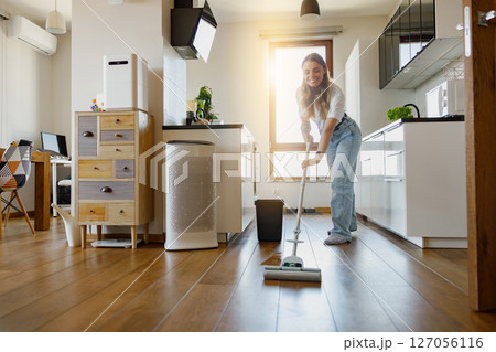 A Charming Woman Happily Engaged in Cleaning the Wooden Floor in a Modern Kitchen Space 127056116
