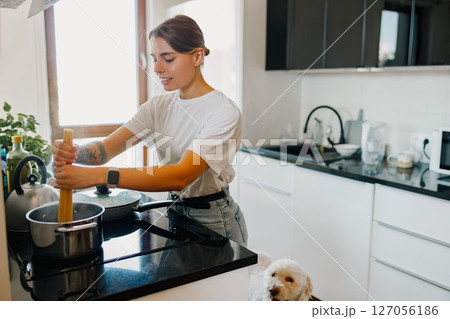 A Young Woman Cooking in a Contemporary Modern Kitchen while Accompanied by her Dog A Young Woman Cooking in a Contemporary Modern Kitchen while Accompanied by her Dog 127056186