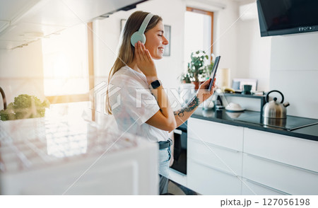 A Woman Joyfully Enjoying Music While in a Modern Kitchen with Stylish Headphones On 127056198