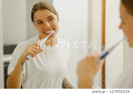 A young woman is happily brushing her teeth in a stylish and modern bathroom setting 127056226