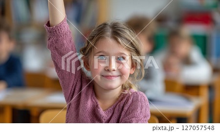 Young girl raises her hand in classroom eager to participate in learning activities with fellow students at a bright school setting 127057548