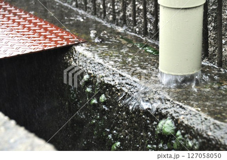 大雨で側溝に流れる雨樋からの雨水 127058050