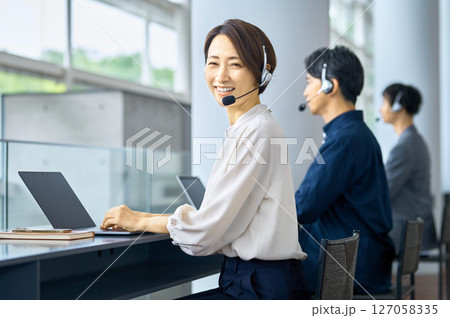 オフィスでチャットするオフィスカジュアルの女性オペレーター 127058335