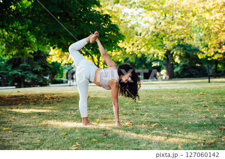 brunette woman doing gymnastics yoga asana on the grass in the park 127060142