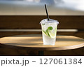 Plastic cup with lime and mint drink on wooden table in sunlight 127061384