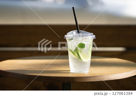 Plastic cup with lime and mint drink on wooden table in sunlight Plastic cup with lime and mint drink on wooden table in sunlight 127061384