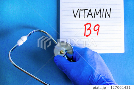 Vitamin B9 folic acid symbol. Concept words Vitamin B9 on beautiful white note. Doctor's hand in blue medical glove. Beautiful blue background. Medical healthy lifestyle Vitamin B9 concept. Vitamin B9 folic acid symbol. Concept words Vitamin B9 on beautiful white note. Doctor's hand in blue medical glove. Beautiful blue background. Medical healthy lifestyle Vitamin B9 concept. 127061431
