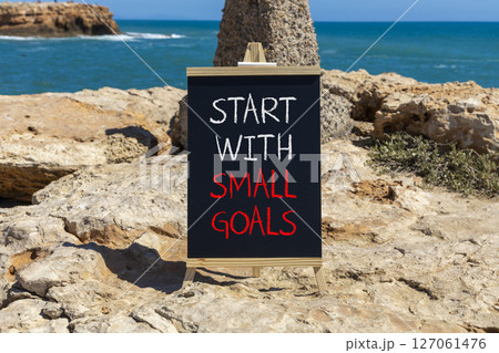 Start with small goals symbol. Concept words phrase Start with small goals on beautiful black blackboard. Beautiful stone blue sea sky background. Business Start with small goals concept. Copy space. Start with small goals symbol. Concept words phrase Start with small goals on beautiful black blackboard. Beautiful stone blue sea sky background. Business Start with small goals concept. Copy space. 127061476