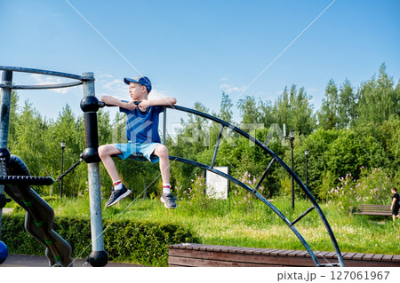 Teenage boy 12 years old in cap and shorts sitting on stairs at top of playground, side view 127061967