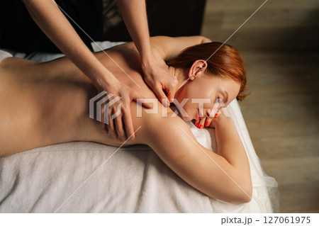 High-angle view of female client getting relaxing back massage from professional massage therapist lying resting on table, experiencing therapeutic wellness at luxurious spa setting, close-up top view 127061975