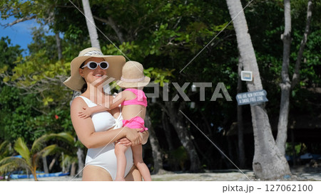Mom strolls along beach with baby daughter under palm trees enjoying summer vacation Mom strolls along beach with baby daughter under palm trees enjoying summer vacation 127062100