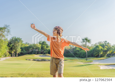 Boy wearing a pilot hat running through the grass with a toy airplane, dreaming of adventures. Childhood, imagination, and freedom concept 127062564