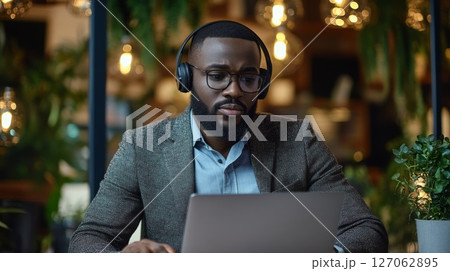 A Black Man Wearing Headphones Working on a Laptop in a Cafe A Black Man Wearing Headphones Working on a Laptop in a Cafe 127062895