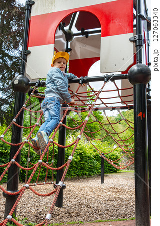 Young child confidently climbing a rope ladder on a playground structure. The child appears focused and determined, showcasing the joy of outdoor play activities. Young child confidently climbing a rope ladder on a playground structure. The child appears focused and determined, showcasing the joy of outdoor play activities. 127063340