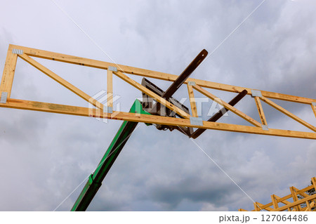Workers operate a lift to install wooden trusses on a building structure as dark clouds loom overhead. Workers operate a lift to install wooden trusses on a building structure as dark clouds loom overhead. 127064486