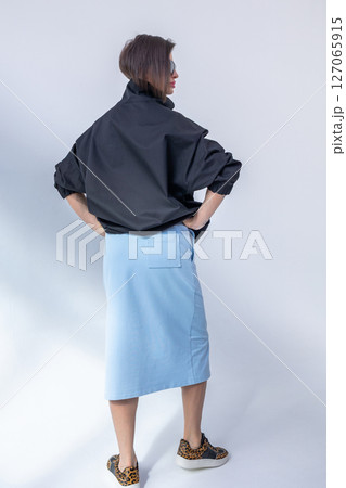 Elegant woman in black windbreaker jacket and light blue skirt on white background. Fashionable female style. Studio photography. Vertical photo. High quality photo 127065915
