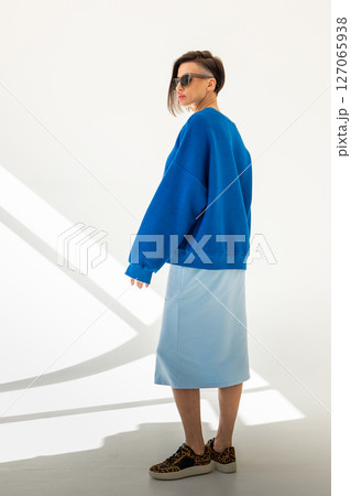 Elegant woman in blue sweatshirt and light blue skirt on white background. Fashionable female style. Studio photography. Vertical photo. High quality photo 127065938