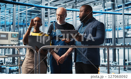 Engineers talking with manager overseeing smart factory, showing collected metrics. Technicians receiving feedback from supervisor in industry 4.0 industrial plant equipped with sensors, camera A 127068092