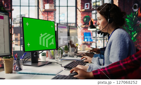 Call center employee working on green screen mockup PC, doing account management in office. Customer support agent in front of chroma key isolated screen computer handling calls, camera B close up Call center employee working on green screen mockup PC, doing account management in office. Customer support agent in front of chroma key isolated screen computer handling calls, camera B close up 127068252