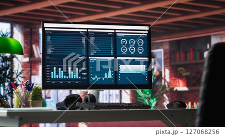 Desktop PC on the wooden desk showcases infographics and client reach data for professional use, analytics on display. Stylish, organized workspace in a bright luxurious loft home. 127068256