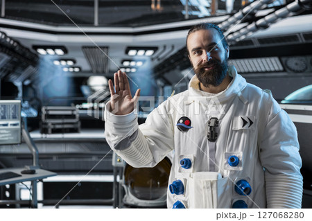 Astronaut waves hand during video call with command center on Earth while stationed aboard spacecraft. Cosmonaut saluting researchers, doing mission update during communication link to ground control 127068280