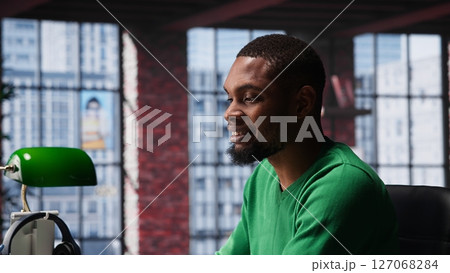 Black teleworker shaking his leg under the desk and acting unsettled, feeling anxious and tense while trying to meet task deadline at home office. Young adult feeling uneasy with ADHD. Camera A. Black teleworker shaking his leg under the desk and acting unsettled, feeling anxious and tense while trying to meet task deadline at home office. Young adult feeling uneasy with ADHD. Camera A. 127068284