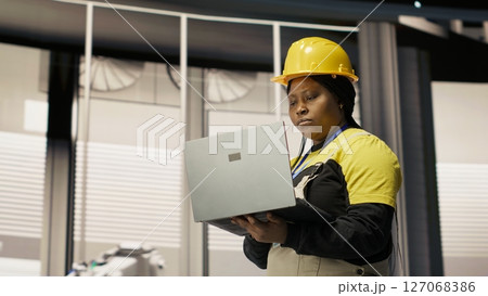 Smart factory mechanic computerizing operations and monitoring energy consumption using laptop. Repairman walking in industry 4.0 plant with notebook, providing technical support, camera B Smart factory mechanic computerizing operations and monitoring energy consumption using laptop. Repairman walking in industry 4.0 plant with notebook, providing technical support, camera B 127068386