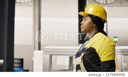 Technician walking in industrial plant, using toolbox to diagnose and fix equipment errors. African american woman in manufacturing factory coordinates repair tasks on assembly lines, camera B Technician walking in industrial plant, using toolbox to diagnose and fix equipment errors. African american woman in manufacturing factory coordinates repair tasks on assembly lines, camera B 127068400