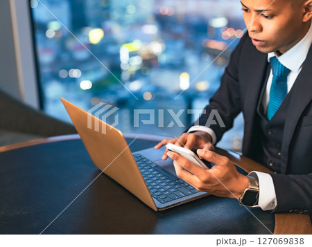 高層ビルのオフィスでノートPCとスマホを使って仕事をするビジネスマン 高層ビルのオフィスでノートPCとスマホを使って仕事をするビジネスマン 127069838