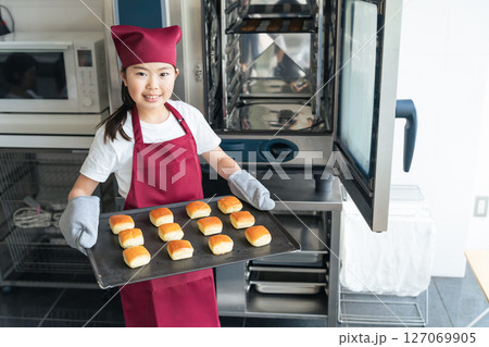 キッチンでオーブンを使ってクッキーを焼く女の子 127069905