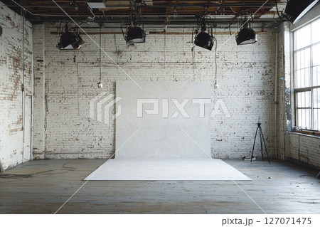 empty industrial studio with white brick walls, wooden floors, and professional lighting equipment, featuring white backdrop for photography 127071475