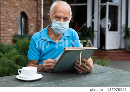 Old man in mask with menu in outdoor cafe Old man in mask with menu in outdoor cafe 127076921