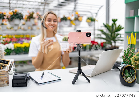 A Caucasian florist broadcasts live from her shop. She is selling a cactus from her collection of plants. 127077748