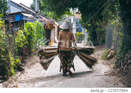 Vietnamese woman in a traditional straw hat carries woven mats made of dyed reeds on cart at a rug factory in a village in Vietnam Vietnamese woman in a traditional straw hat carries woven mats made of dyed reeds on cart at a rug factory in a village in Vietnam 127077804